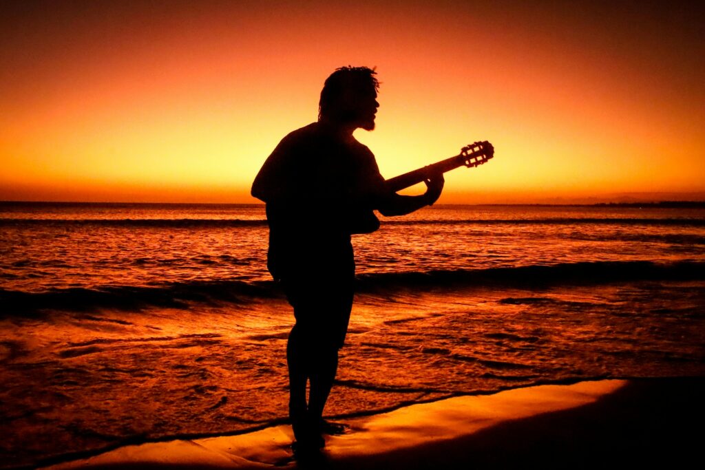A peaceful silhouette of a musician playing guitar on the beach during sunset.